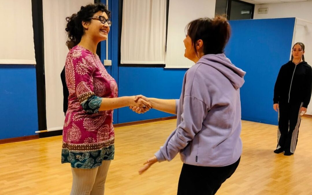 Ragazze durante un esercizio di teatro in sala prove, si stringono la mano mentre lavorano sulla relazione scenica.